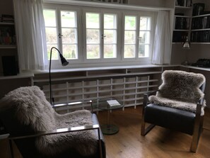 Una habitación con un ventanal grande, un radiador, un escritorio, una silla y una estantería.