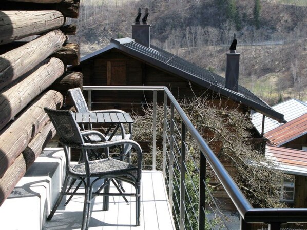 Una terraza de madera con barandilla de metal, una silla de mimbre y una mesa.