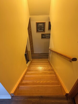 Eine Holztreppe mit Handlauf, die zu einer Zwischenebene mit gerahmten Bildern an der Wand führt.