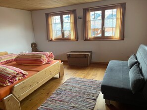 Una habitación con una cama de madera, un sofá, una mesita y dos ventanas con cortinas.