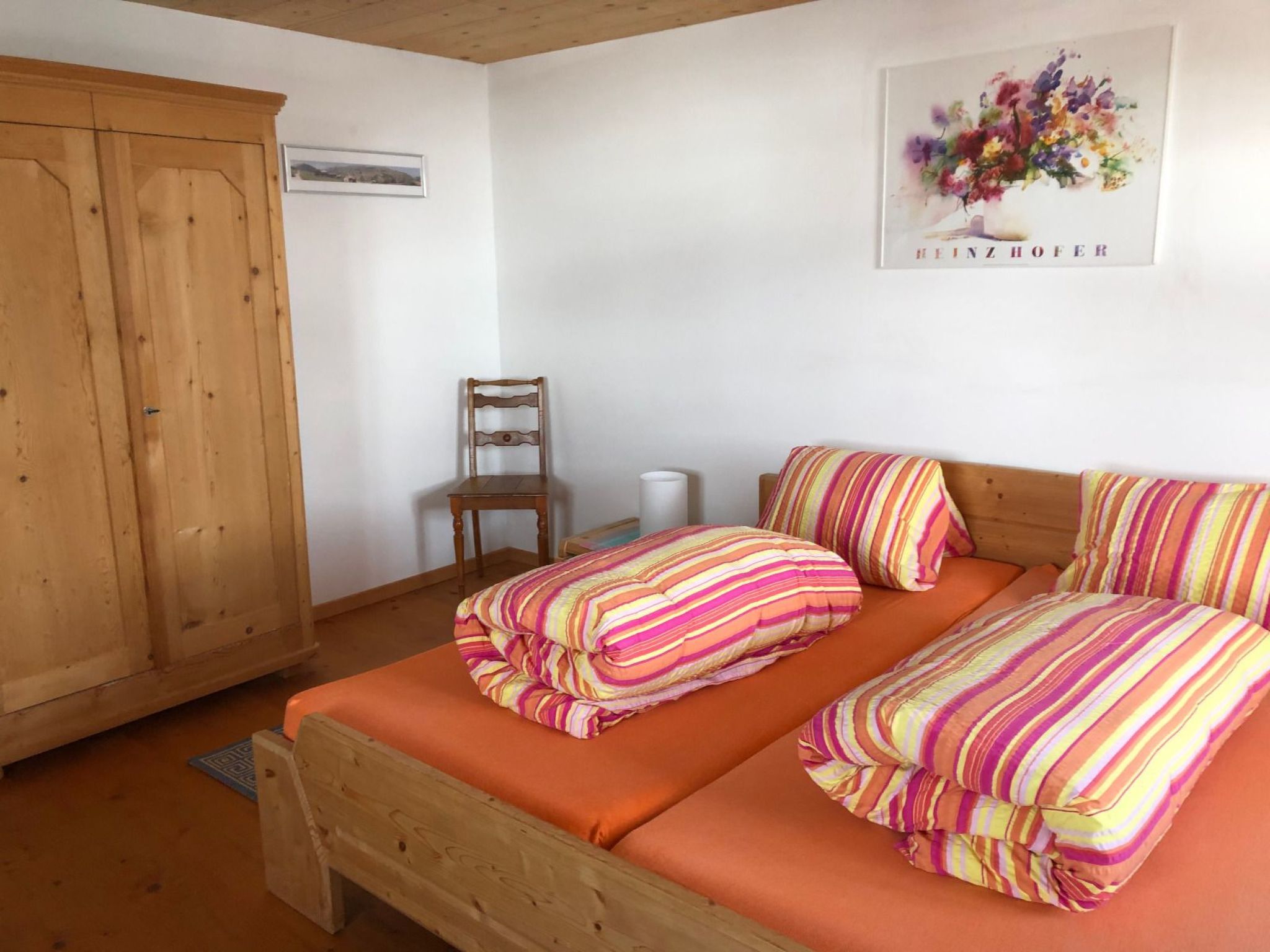 A bedroom with a wooden bed, striped bedding, a wooden wardrobe, and a framed picture on the wall.