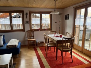 Un'accogliente sala da pranzo con tavolo e sedie in legno, un tappeto a righe rosse e gialle e ampie finestre con tende in pizzo.