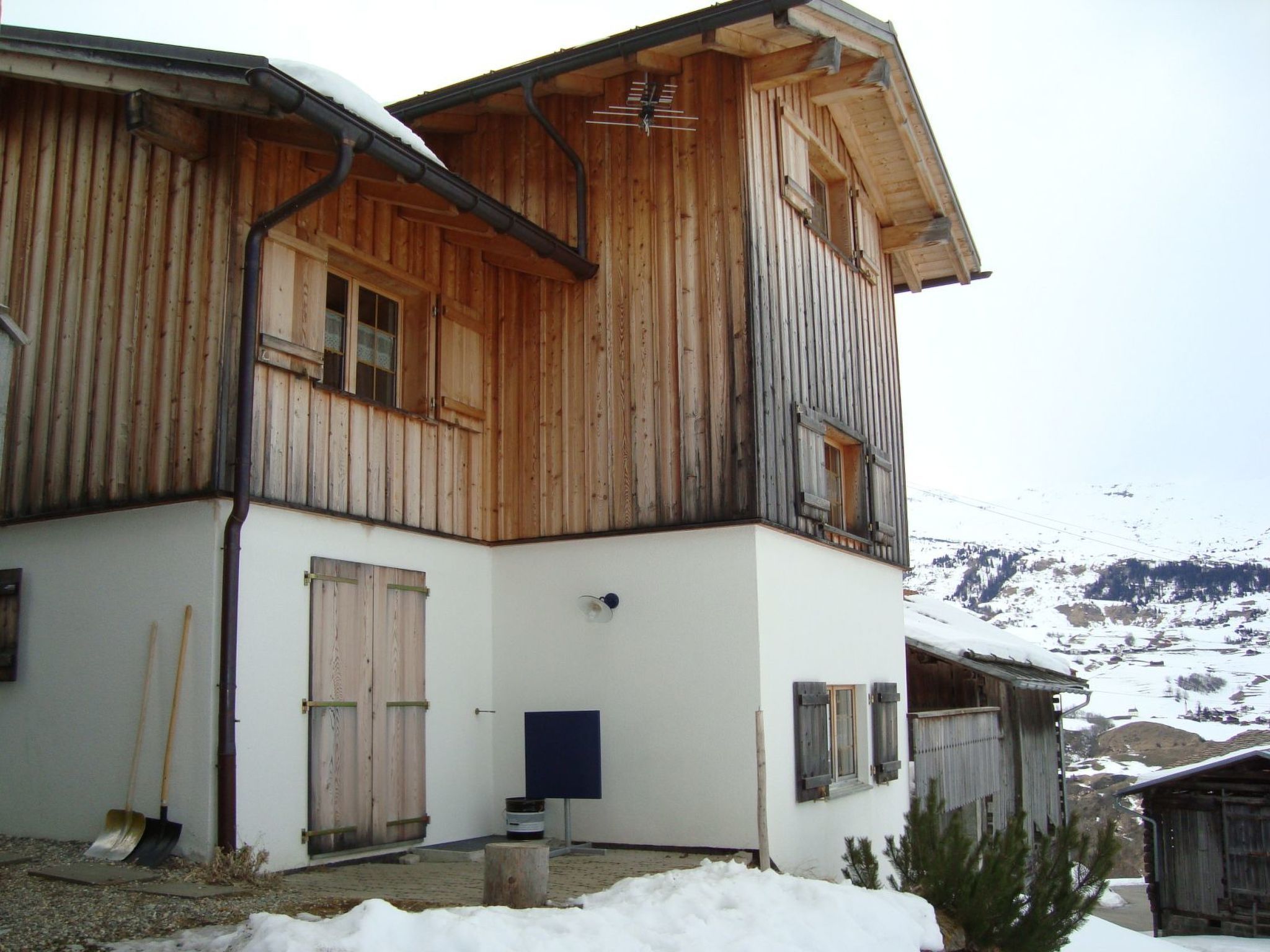 Un bâtiment en bois à deux étages, doté d’un toit en pente, d’une cheminée bien visible et d’un sol recouvert de neige.