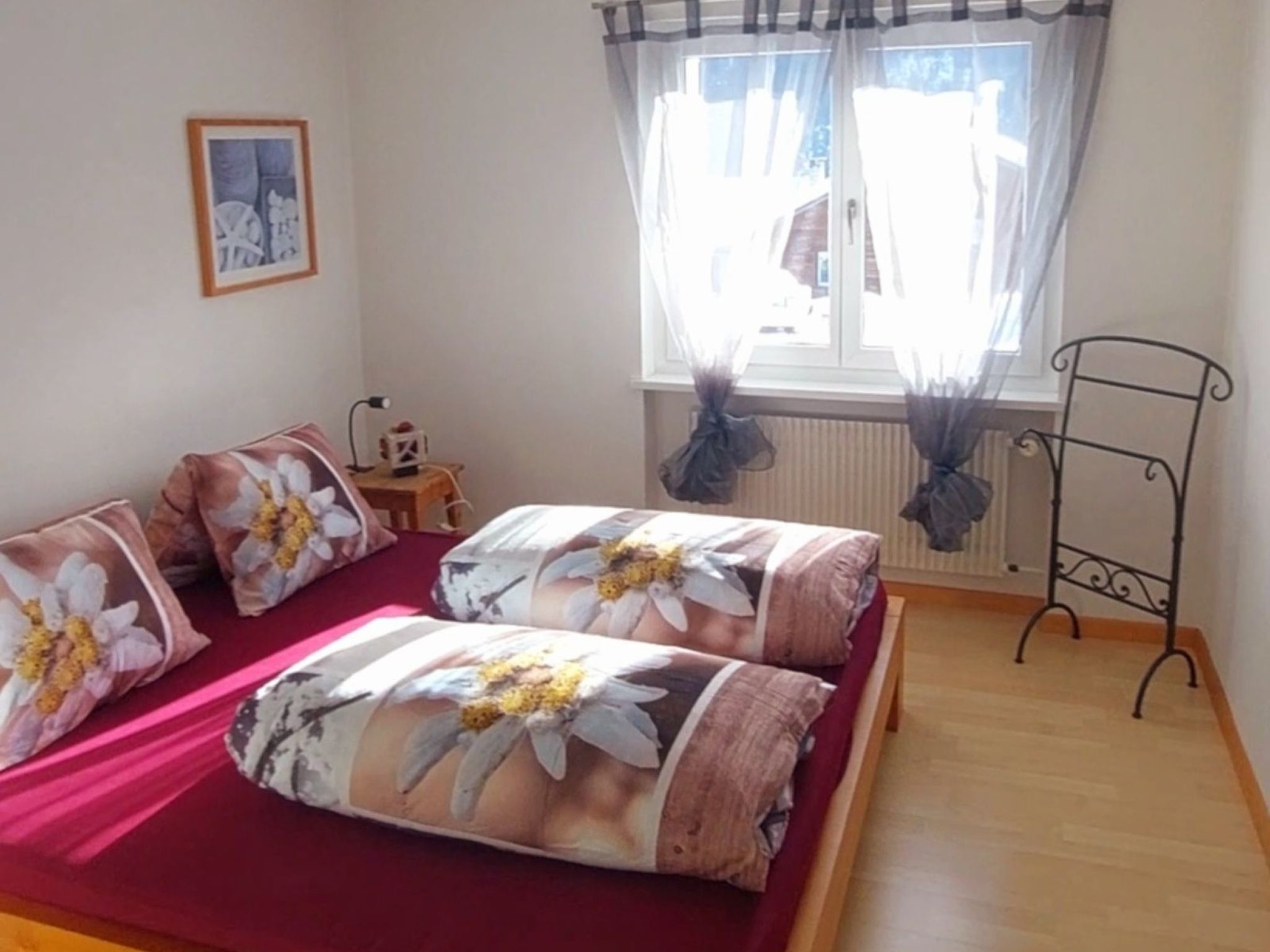 A room with a bed, a small table with a lamp, a chair, and a window with curtains.