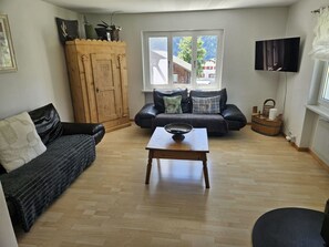 A living room with a wooden floor, a sofa, a coffee table, and a television mounted on the wall.