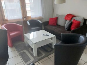 Ein Wohnzimmer mit einer Couch, zwei Sesseln, einem Couchtisch und einem Fenster mit Vorhängen.