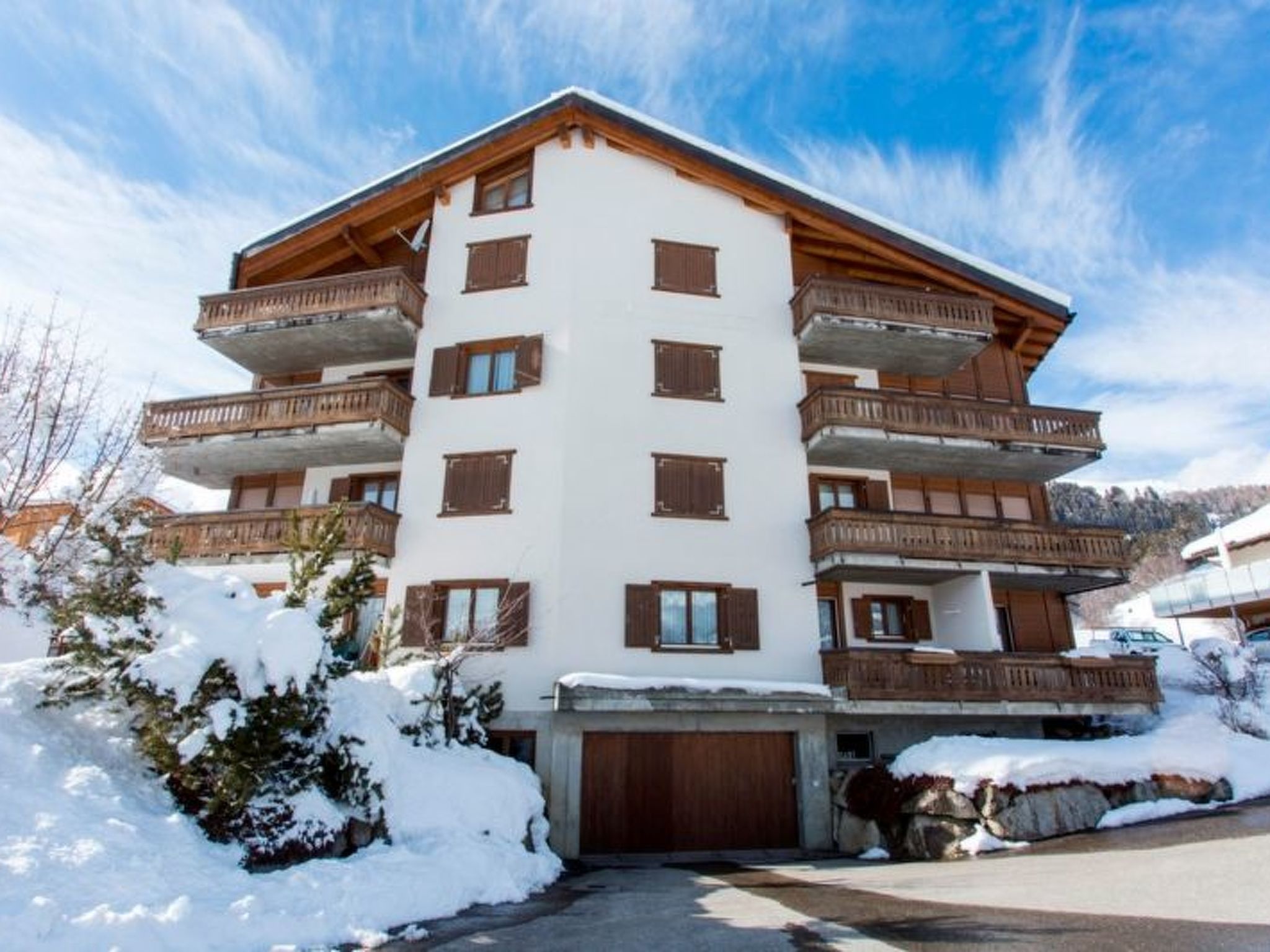 Un hotel de varios pisos con balcones, un garaje y paisajes nevados.