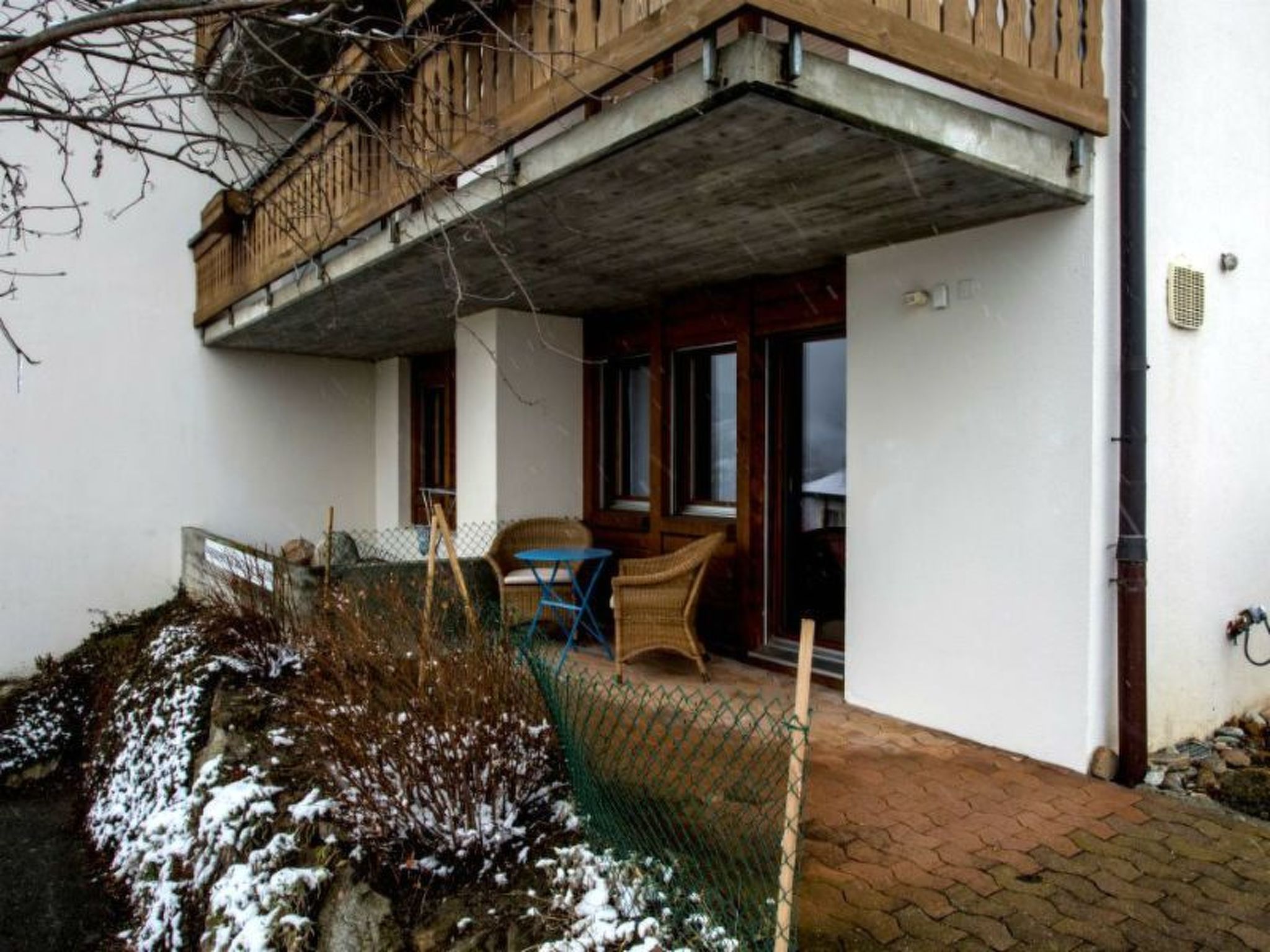 Ein Wohngebäude mit Balkon, überdachter Außenlounge und kleinem Schneebeet.