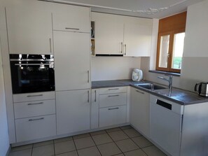 Eine moderne Küche mit weißen Schränken, einem Backofen, einer Kaffeemaschine und einem Fenster mit Jalousien.