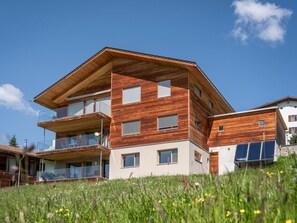 A modern multi-story building with wooden exterior panels, balconies, and large windows.