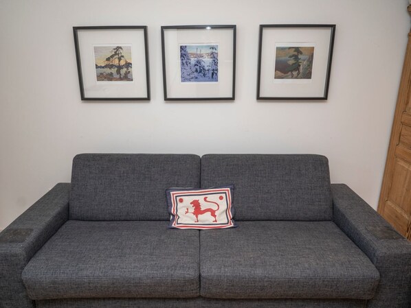 A grey sofa with a single decorative pillow in front. Three framed artworks are hung on the wall above the sofa.