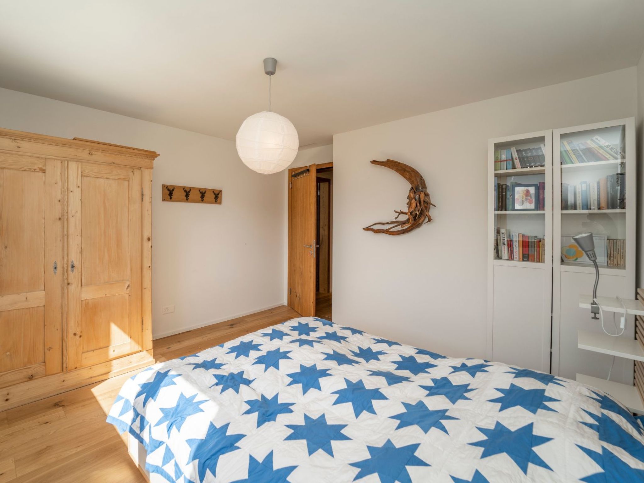 Een slaapkamer met een bed, een houten garderobe, een deur, een wandplank en een plafondlamp.