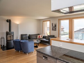 Ein modernes Wohnzimmer mit einer Couch, blauen Sesseln, einem Couchtisch, einem Kamin und einer Küchenzeile mit Herd.