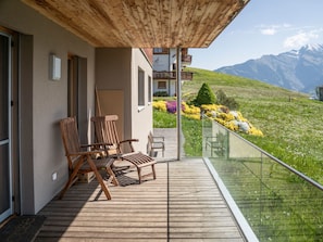 Eine Holzterrasse mit Sitzgelegenheit, einer Glastrennwand und Blick auf die Berge.