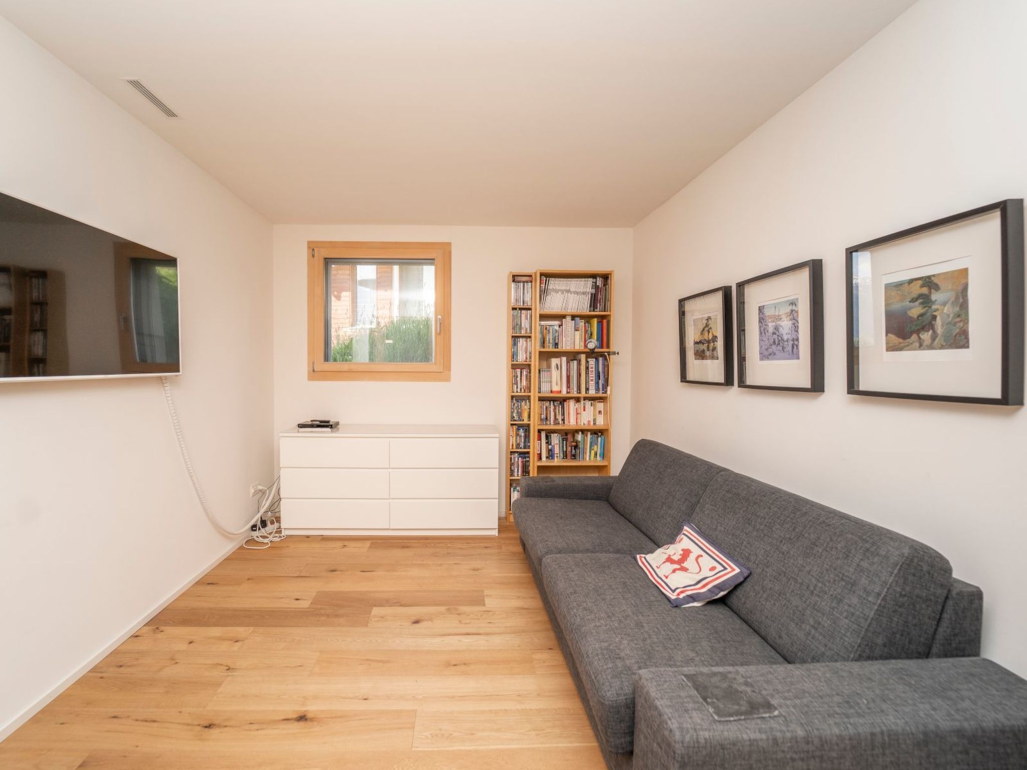 Ein modernes Wohnzimmer mit einem grauen Sofa, einem weißen Schrank, einem Bücherregal und gerahmten Bildern an der Wand.