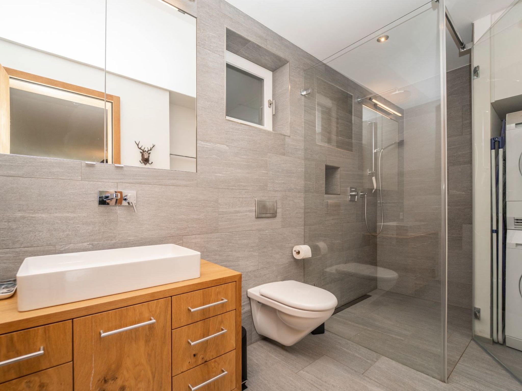 A modern bathroom with a large mirror, a wooden vanity, a toilet, and a glass-enclosed shower area.