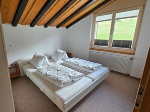 Une petite chambre à coucher composée d’une seule pièce, avec un plafond en pente, une fenêtre équipée de stores et un radiateur.