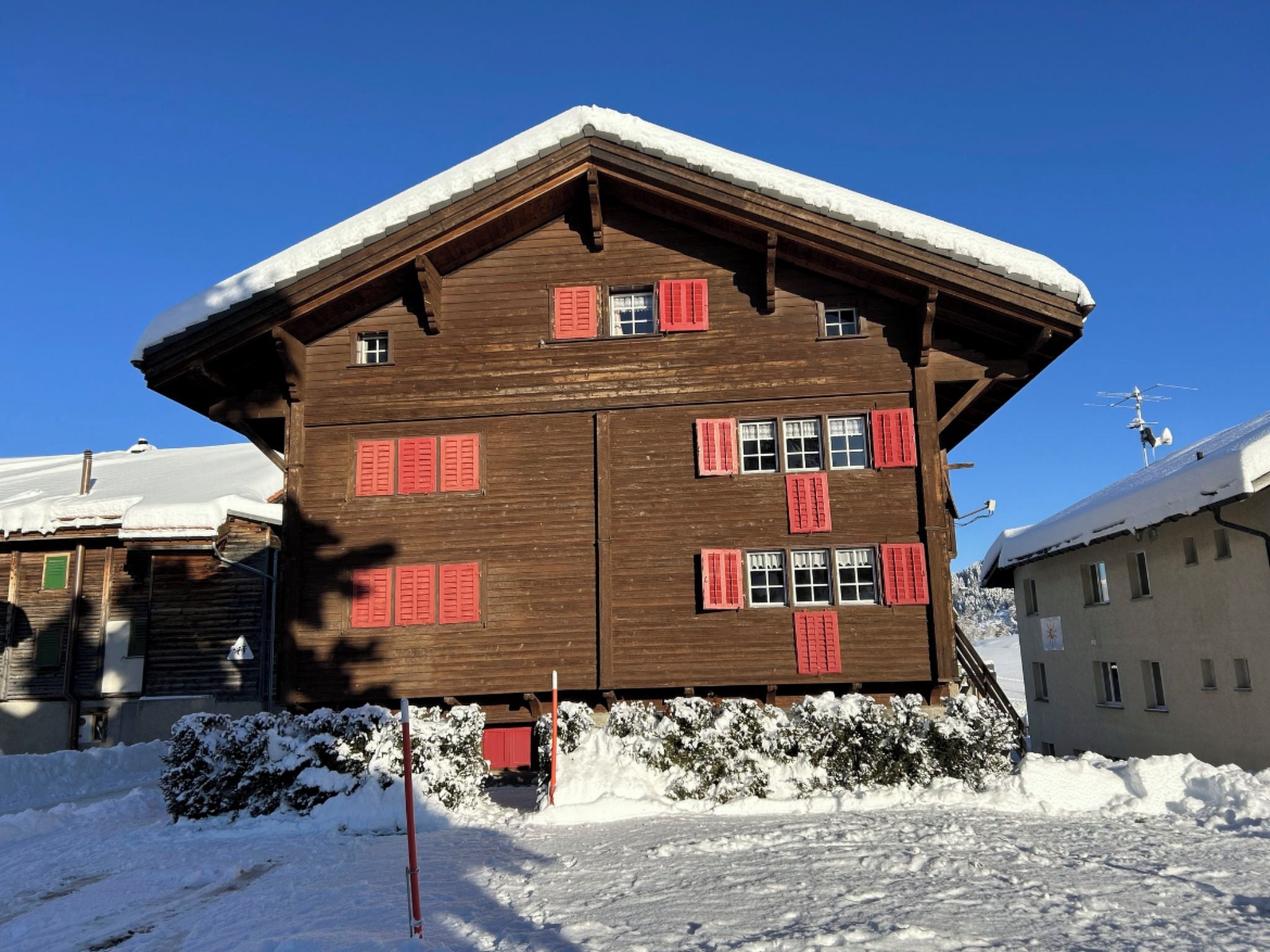 A wooden chalet with multiple windows and red shutters, surrounded by snow.
