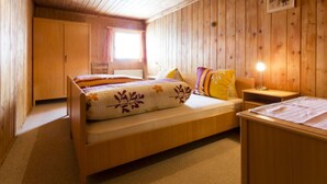 Ein Zimmer mit Holzboden, einem Bett, einem Nachttisch und einem Fenster.