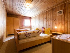 A wooden room with a bed, bedside table, and a window.