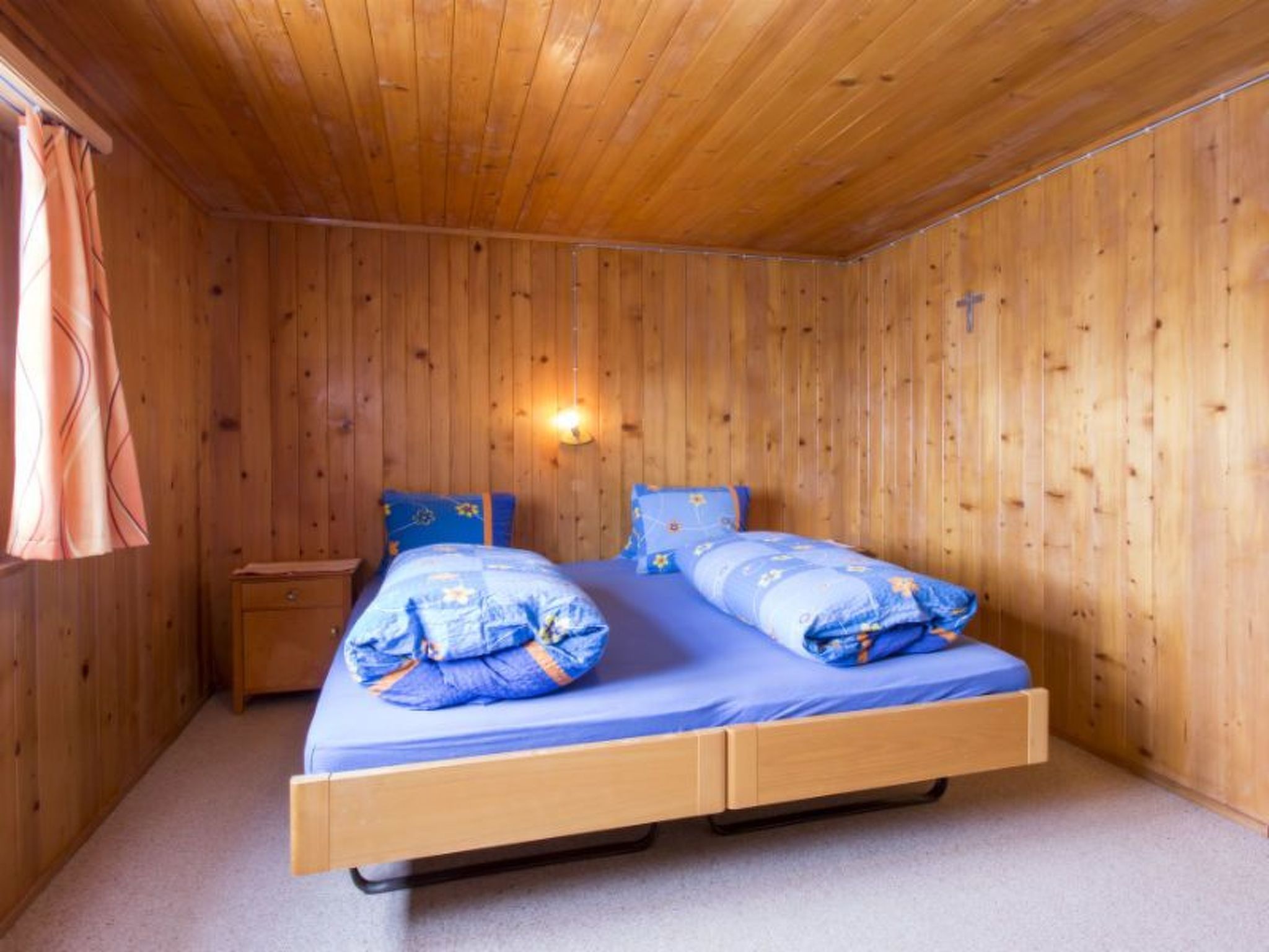 A wooden-paneled room with a bed, a nightstand, and a wall-mounted light fixture.