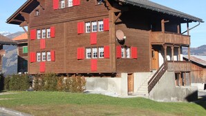 Ein mehrgeschossiges Holzhaus mit roten Fensterläden, einem Balkon und einer Satellitenschüssel.