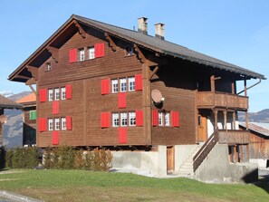 A multi-story wooden building with red shutters, a balcony, and a satellite dish.