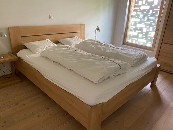 Ein hölzernes Bett mit weißer Bettwäsche in einem Zimmer mit Holzboden und einem Fenster.