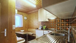 A compact kitchen with wooden walls, a sink, a stove, and a window with curtains. - Genoveva Sax, Obersaxen-Meierhof, (Obersaxen), 34065B by Interhome (Obersaxen Affeier)