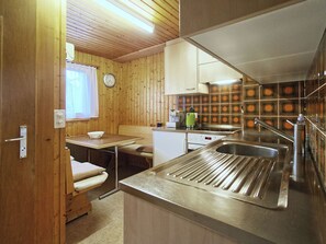 A compact kitchen with wooden walls, a sink, a stove, and a window with curtains. - Genoveva Sax, Obersaxen-Meierhof, (Obersaxen), 34065B by Interhome (Obersaxen Affeier)