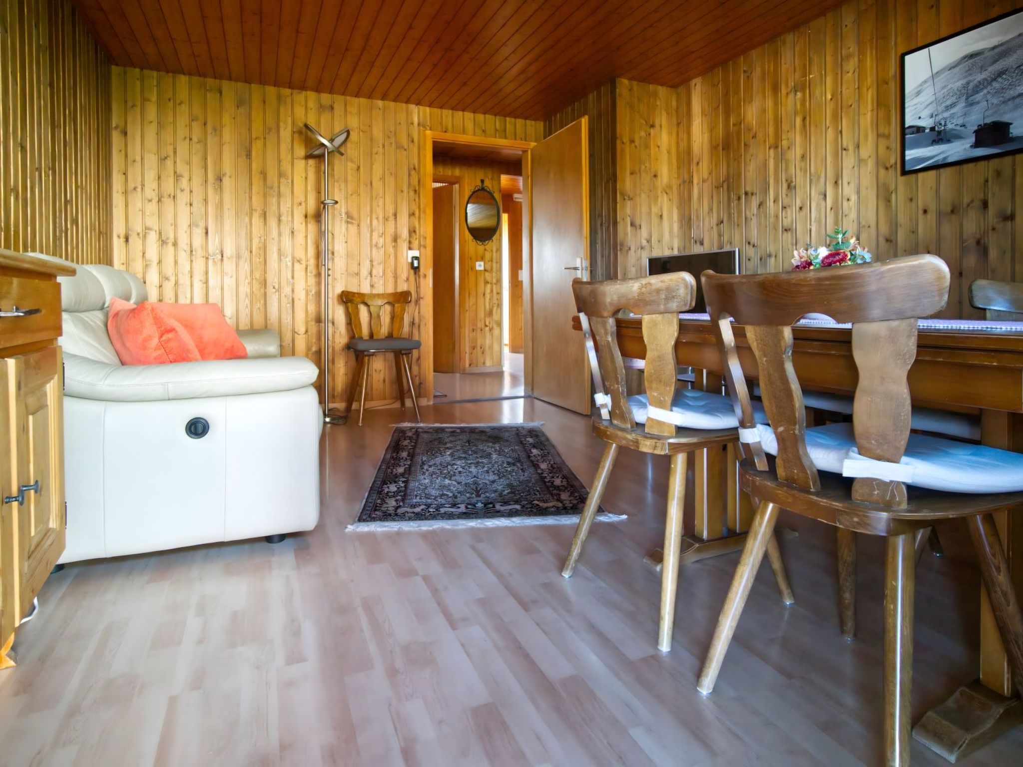 A wooden interior with a sofa, chairs, a dining table, and a television.