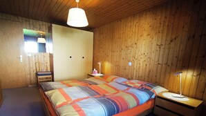 A wooden-paneled bedroom with a bed, bedside tables, and a nightstand. - Genoveva Sax, Obersaxen-Meierhof, (Obersaxen), 34065B by Interhome (Obersaxen Affeier)