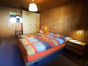 Ein Schlafzimmer mit einem Bett, Nachttischen, einem Sessel, einem Kleiderschrank und einer Hängeleuchte.