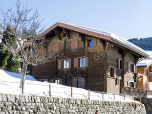 Eine Holzhütte mit einer Steinsäule vor verschneiter Landschaft.