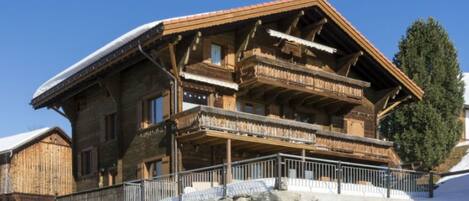 Un chalet en bois avec un escalier en pierre menant à l’entrée, entouré de neige.
