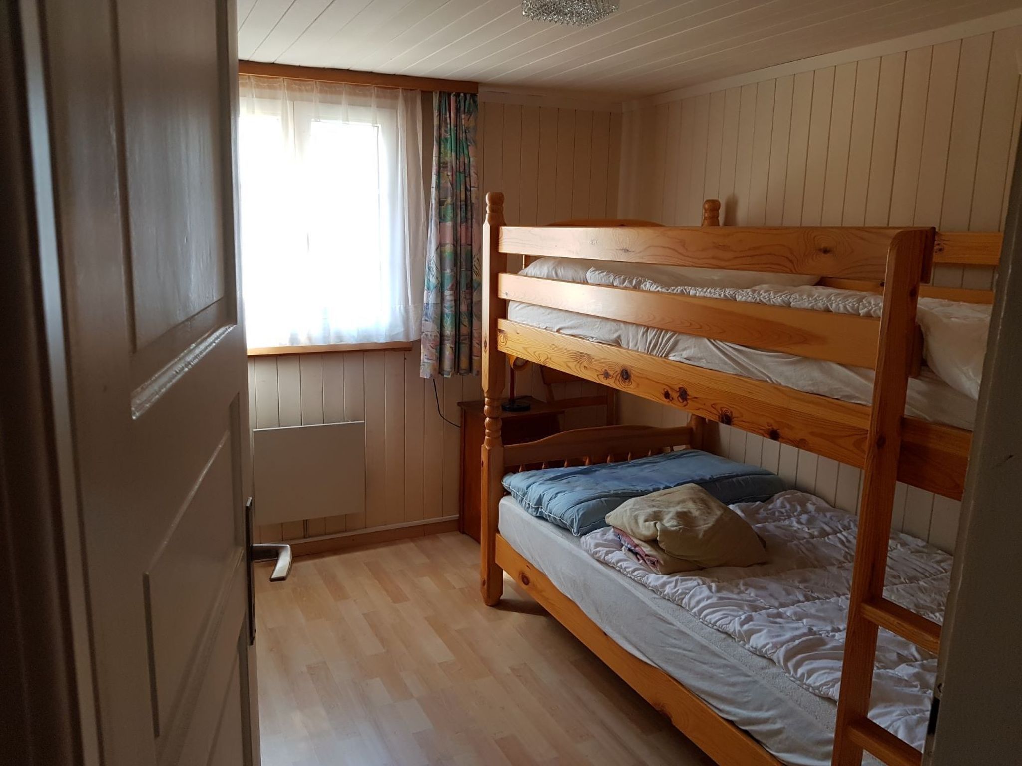 Ein Schlafraum mit Etagenbetten, einem Fenster, Holzwänden und einer Heizung.
