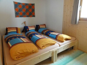 A single bed with a wooden frame and a mattress, a wall-mounted light fixture, and a window with curtains.