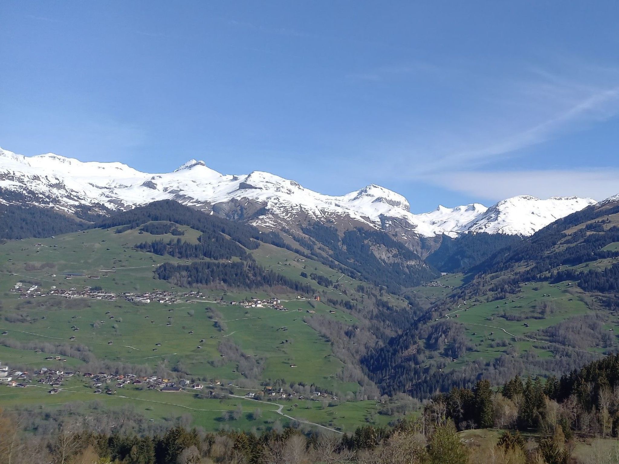 A mountainous landscape with snow-capped peaks, a valley with scattered buildings, and a clear sky.