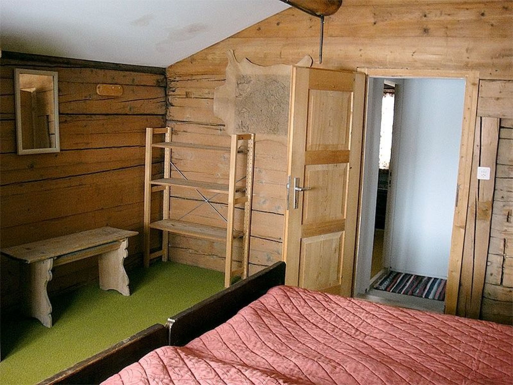 Quarto com cama, um banco, uma escada e uma porta que dá para outro cômodo.