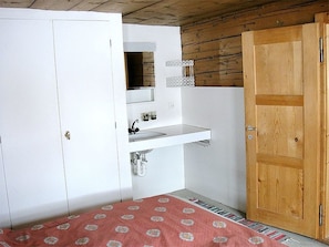 A small, compact room with a white wardrobe, a wooden door, a white sink, and a patterned rug. - Ferienhaus Casa Cadruvi, Obersaxen-Giraniga, (Obersaxen), 34077B by Interhome (Obersaxen Affeier)