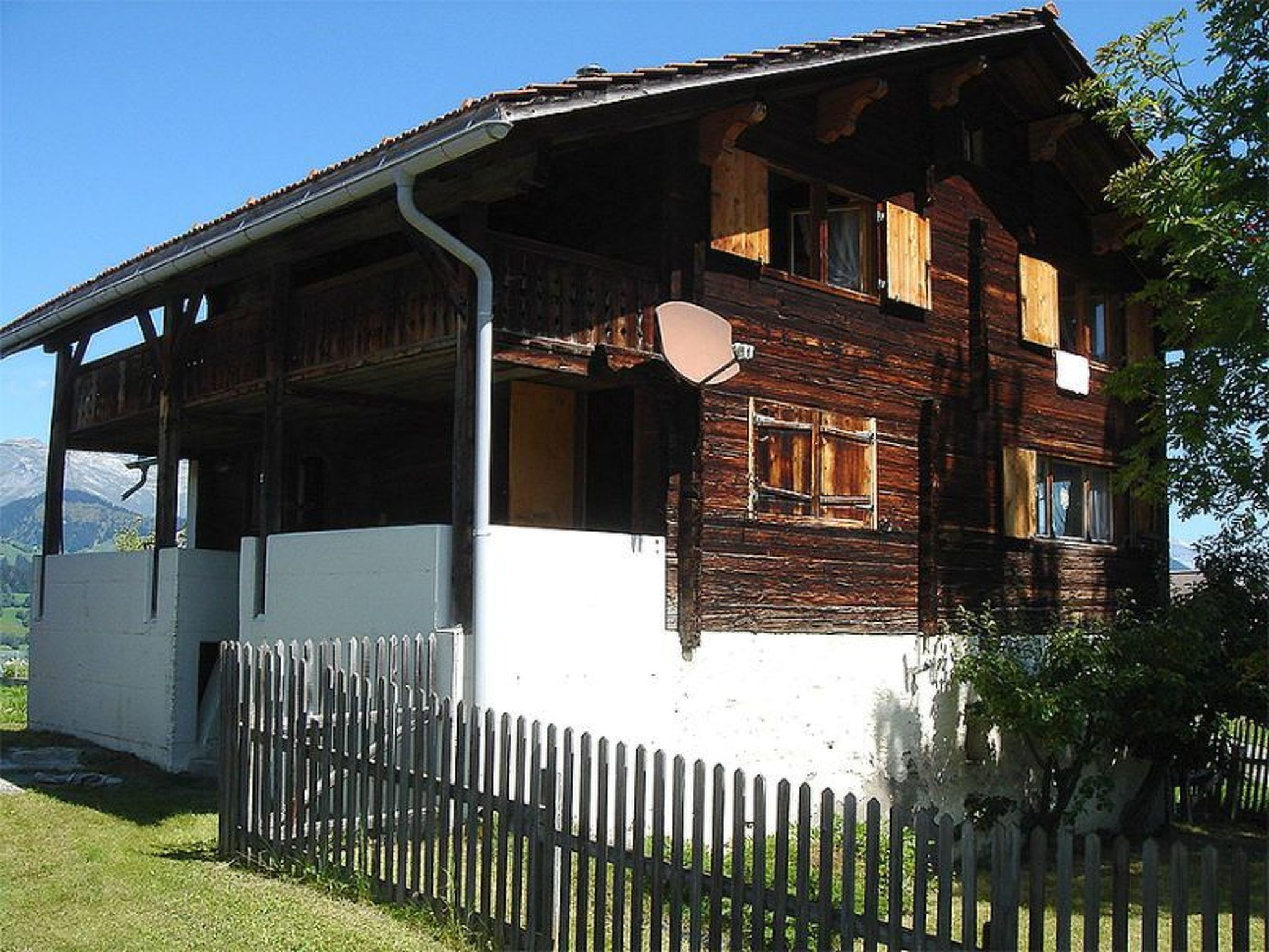 A wooden house with a balcony, a white fence, and a mountainous backdrop.