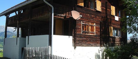 Une maison en bois avec un balcon, une clôture blanche et un paysage montagneux en arrière-plan.