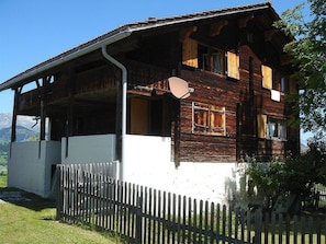 A wooden house with a balcony, a white fence, and a mountainous backdrop. - Ferienhaus Casa Cadruvi, Obersaxen-Giraniga, (Obersaxen), 34077B by Interhome (Obersaxen Affeier)