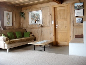 A room with a wooden door, a sofa with green cushions, a coffee table, and framed pictures on the wall. - Ferienhaus Casa Cadruvi, Obersaxen-Giraniga, (Obersaxen), 34077B by Interhome (Obersaxen Affeier)