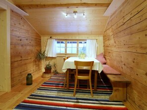 Ein gemütliches Zimmer mit Holzvertäfelung, einem Esstisch mit Stühlen, einer Bank und einem Fenster mit Vorhängen.