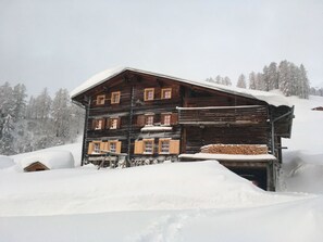 Eine mehrstöckige Holzhütte mit geneigtem Dach, umgeben von schneebedeckten Bäumen.
