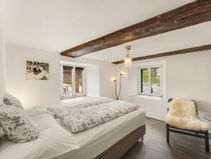 A bedroom with a large bed, two windows, a wooden ceiling beam, and a chair. - Pacifica und Romantica in Cumpadials, (Cumpadials), 76002B by Interhome (Cumpadials)