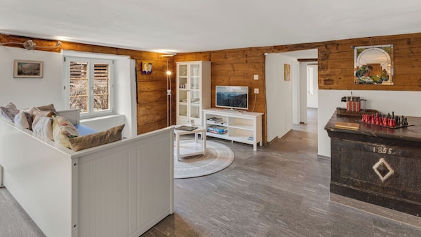 Una sala de estar con televisor, paredes de madera, un mueble blanco y chimenea.