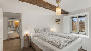 Un dormitorio con una cama grande, una mesita de noche con lámpara, una ventana con vistas y una viga de techo de madera.