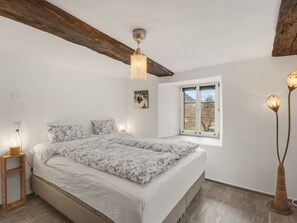 Ein Schlafzimmer mit einem Bett, einem Nachttisch, einer Stehlampe, einem Fenster und einem Bild an der Wand.